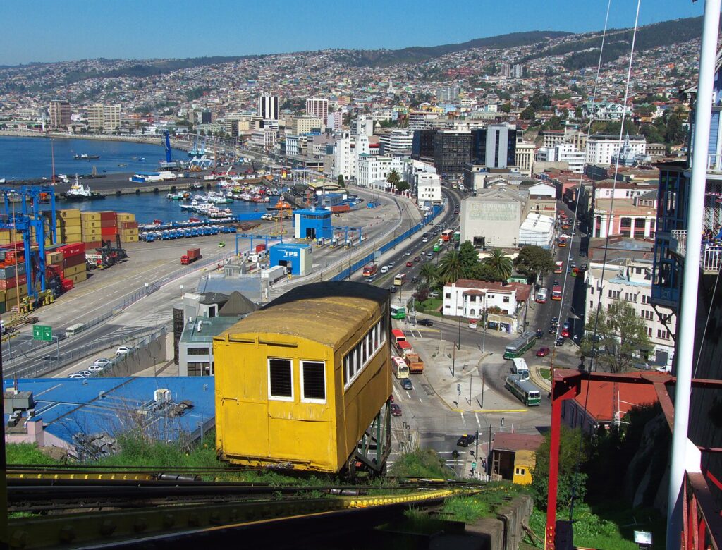 View of central Valparaíso, Chile, from the top of the Artillería funicular (incline) (Ascensor Artillería). At the bottom of the funicular are two trolleybuses at the Aduana terminus of the Valparaíso trolleybus system. The city's remaining funiculars and its trolleybuses have both been declared National Historic Monuments.